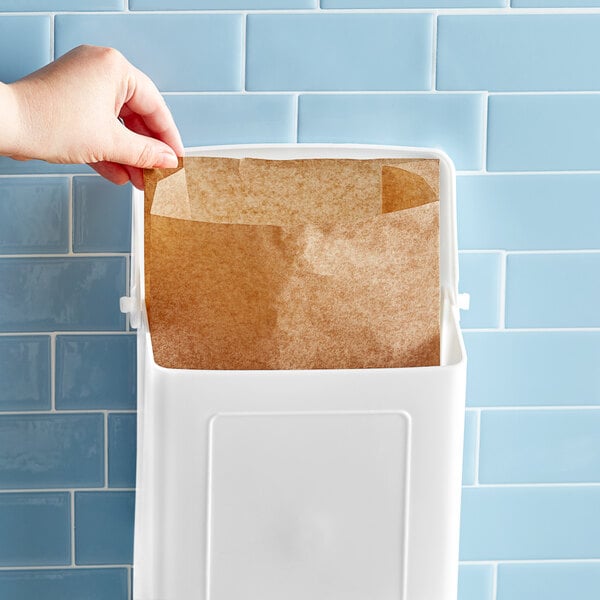 A hand putting a brown paper bag in a white container with brown paper inside.