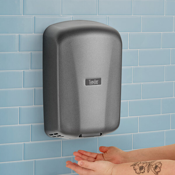 A person using a grey Excel ThinAir hand dryer with a logo on it to dry their hands.