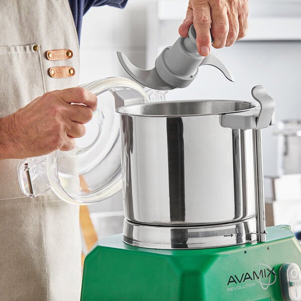 A person using an AvaMix stainless steel bowl with an "S" blade in a food processor.
