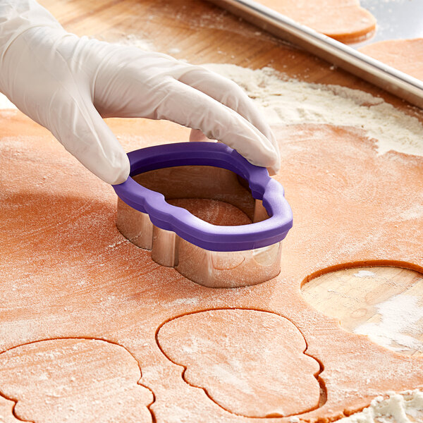 A person's gloved hand uses a Wilton metal skull cookie cutter to cut out cookies.