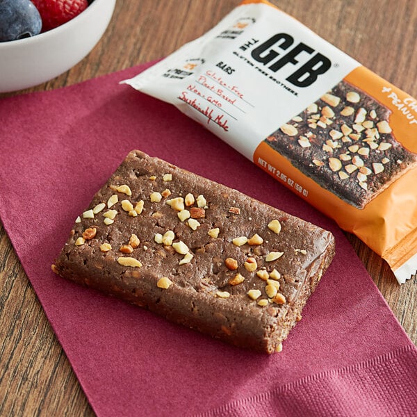 A GFB chocolate peanut butter bar with nuts on top next to a bowl of berries.