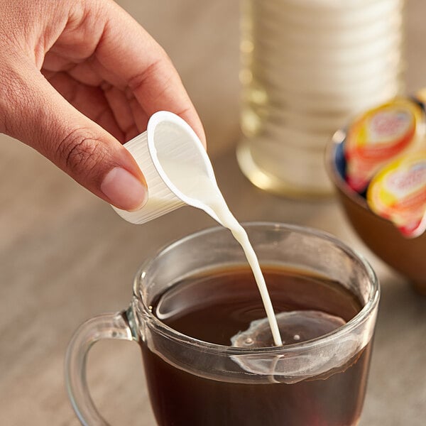 A person pouring Nestle Coffee-Mate Hazelnut non-dairy creamer into a cup of coffee.