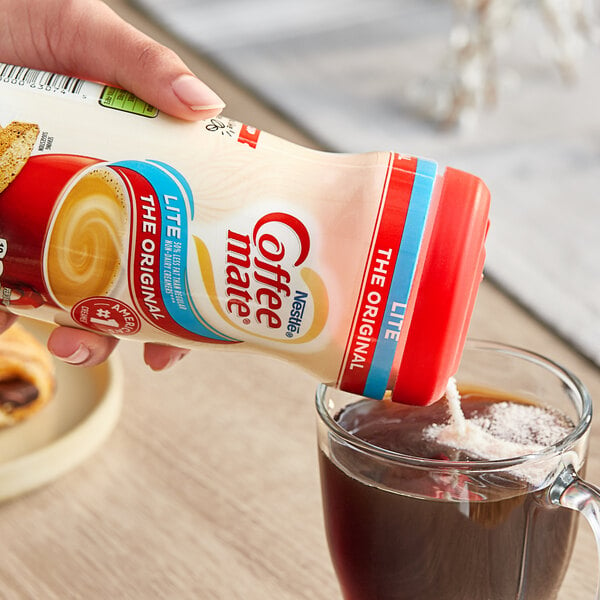 A hand pouring Nestle Coffee-Mate Lite coffee creamer into a cup of coffee.
