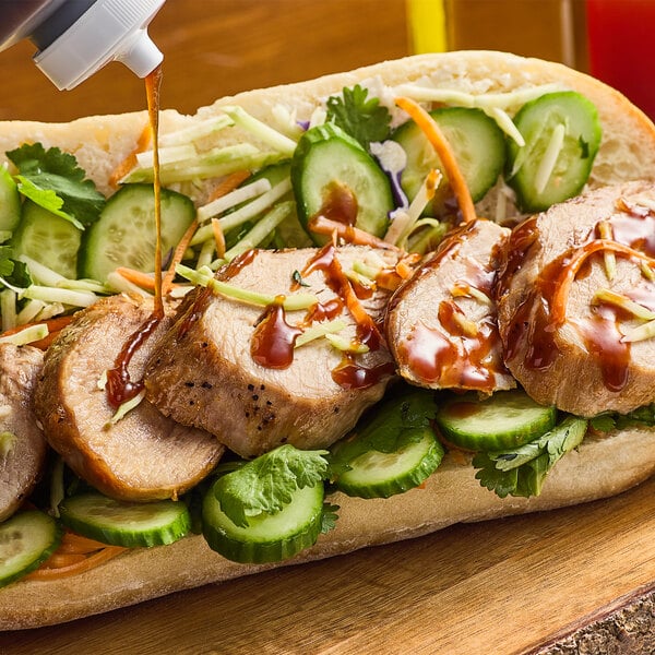 A sandwich with Minor's Lemongrass BBQ sauce on meat and vegetables on a wooden cutting board.