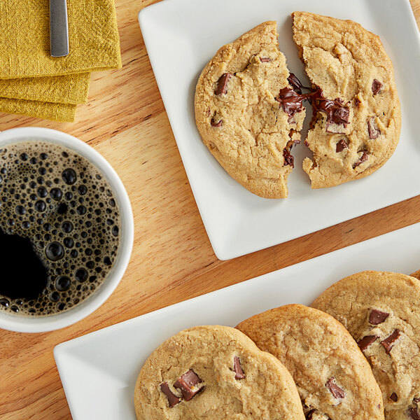 A plate of Otis Spunkmeyer milk chocolate chunk cookies on a table with a cup of coffee.