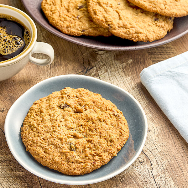 A plate of Otis Spunkmeyer Sweet Discovery oatmeal raisin cookies on a table with a cup of coffee.