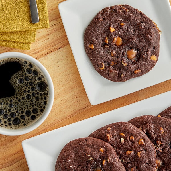 A plate of Otis Spunkmeyer chocolate turtle cookies with a cup of coffee on a table.