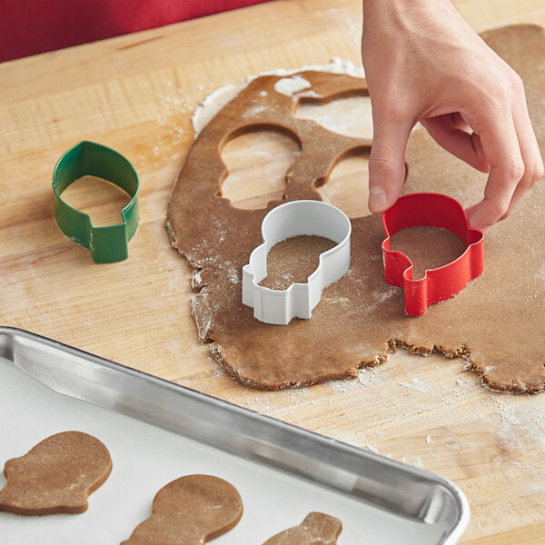 A hand using a white Wilton holiday cookie cutter to cut gingerbread cookies.