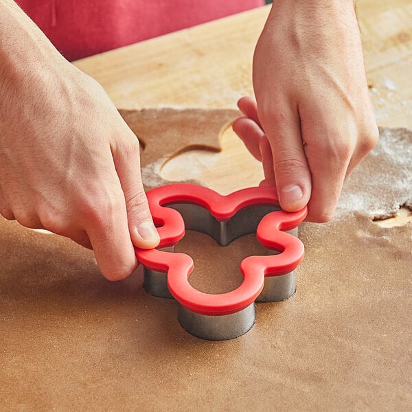 A person's hands cutting a cookie with a Wilton metal gingerbread man cookie cutter.