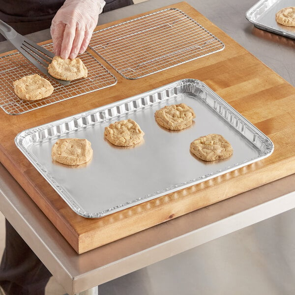 A hand in gloves cutting cookies on a Baker's Lane foil cookie sheet.