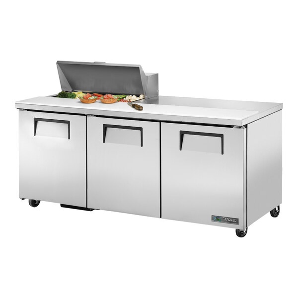 A True commercial stainless steel refrigerated sandwich prep table with 3 doors and food on top.
