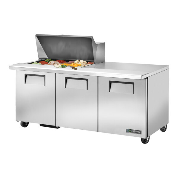 A True 3 Door Mega Top Refrigerated Sandwich Prep Table with a stainless steel counter top and large stainless steel doors filled with food.