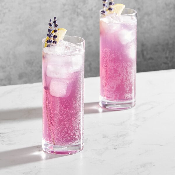 Two Della Luce Origins beverage glasses filled with pink liquid, ice, and lavender and lemon.