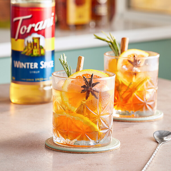 Two glasses of Torani Winter Spice flavoring syrup in orange drinks with cinnamon sticks.
