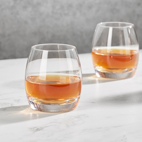 Two Della Luce Avalon rocks glasses filled with brown liquid on a marble surface.