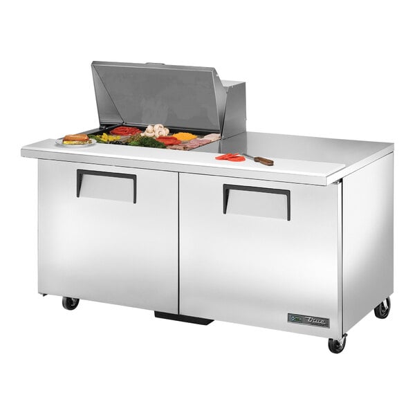 A True stainless steel 2 door refrigerated sandwich prep table with food on the counter.