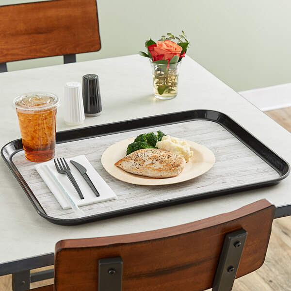 A Dinex woodgrain non-skid fiberglass tray with a plate of food, a fork, and a knife.