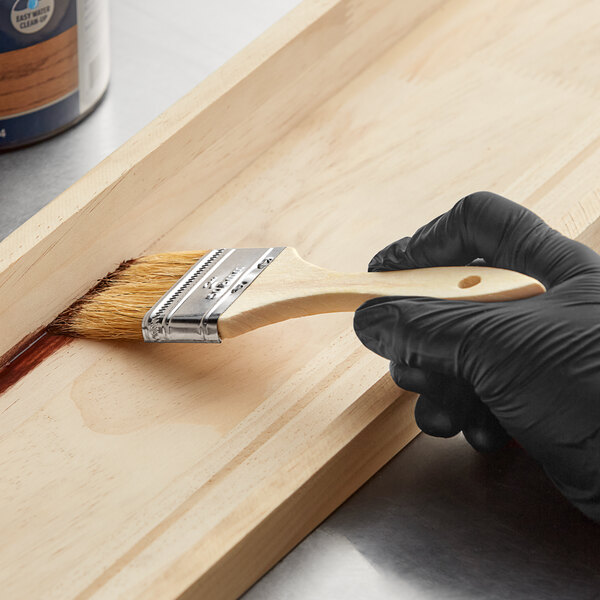 A person using a Midwest Rake 2" Bristle Chip Brush to paint a wooden surface.