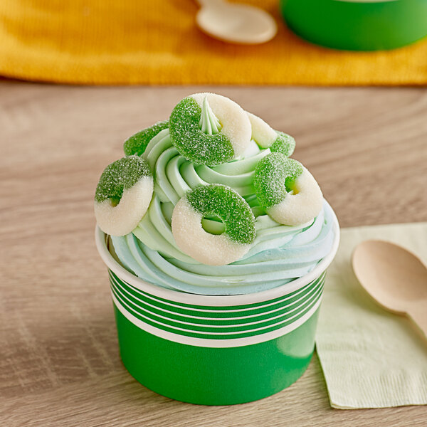 A cup of ice cream with green and white frosting and green apple gummi rings on top.