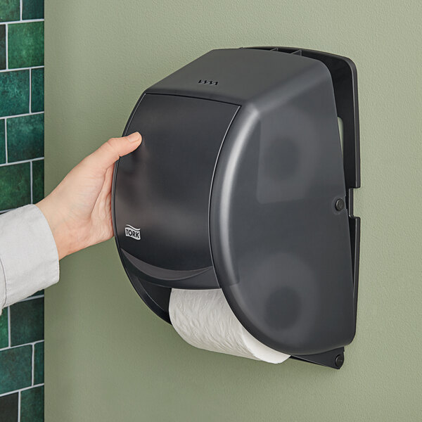 A hand holding a black Tork toilet paper roll.