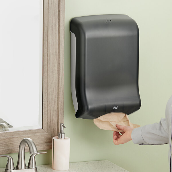 A woman using a black Tork hand towel dispenser.