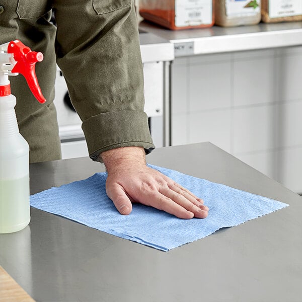 A person cleaning a table with a blue Tork paper towel.
