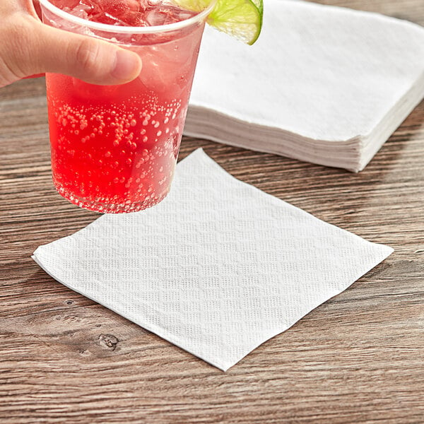 A hand holding a glass with a drink on a Tork white beverage napkin.