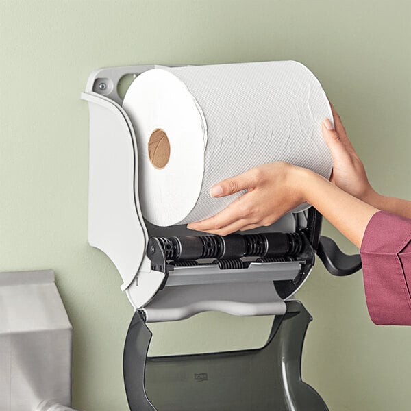 A person holding a roll of white Tork paper towels.