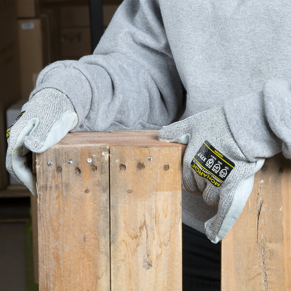 A person wearing Cordova Monarch gray cut-resistant gloves holding a piece of wood.