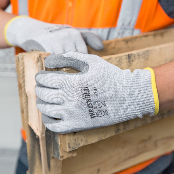 A person wearing Cordova cut-resistant work gloves with gray palms holding a piece of wood.