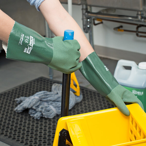 A person wearing Cordova ActivGrip green gloves holding a yellow bucket.
