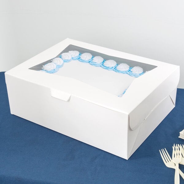A white Baker's Mark bakery box with blue and white frosted cakes inside.