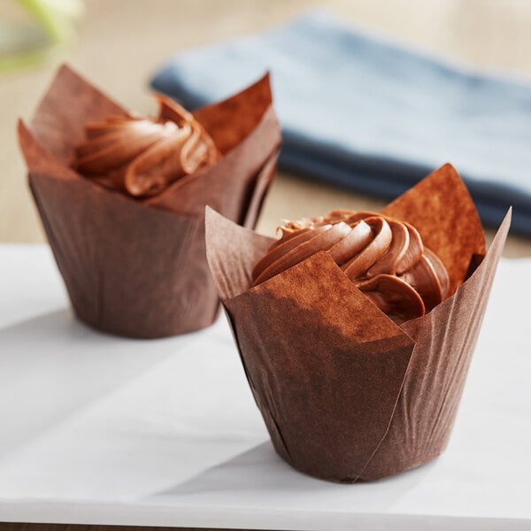 Two chocolate cupcakes in Baker's Mark tulip baking cups with brown frosting swirls.