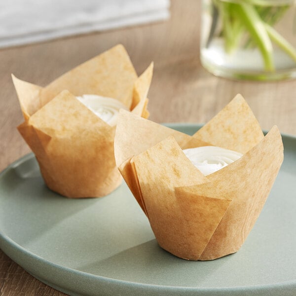 Two Baker's Mark unbleached natural Kraft tulip baking cups with cupcakes inside on a plate.