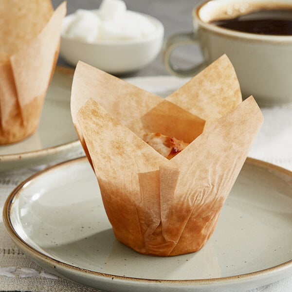 A Baker's Mark tulip cupcake wrapper on a plate with a cup of coffee.