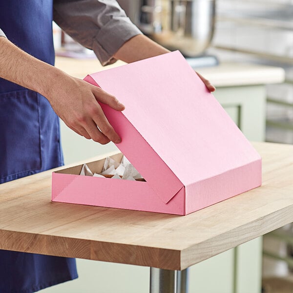 A person opening a Baker's Mark pink bakery box.