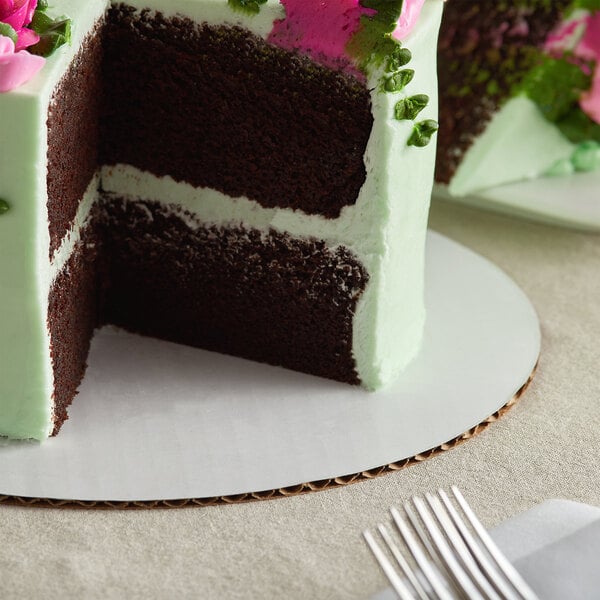 A Baker's Mark white corrugated cake circle with a chocolate cake with green frosting and pink flowers on top.