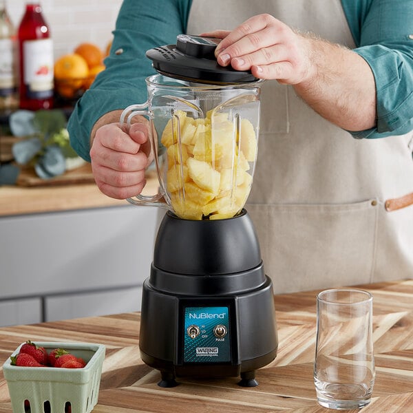 A man using a Waring commercial blender to make a fruit smoothie.