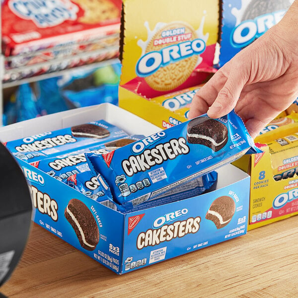 A person's hand holding a box of Nabisco Oreo Cakesters snack packs.