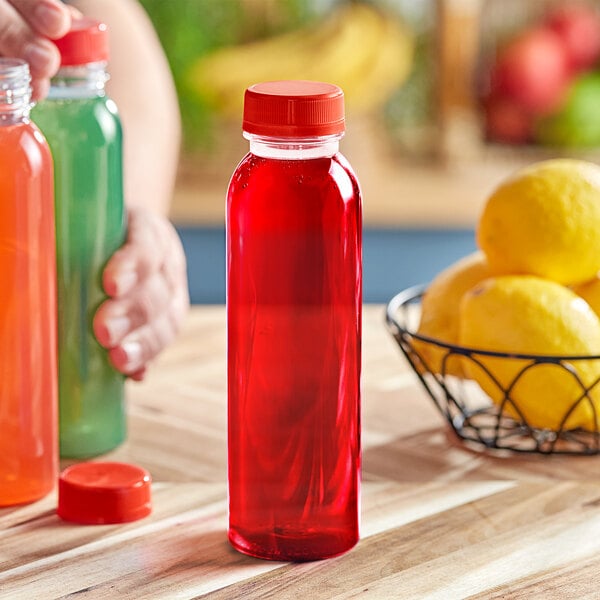A person holding a 12 oz. round clear juice bottle with red liquid next to a lemon.