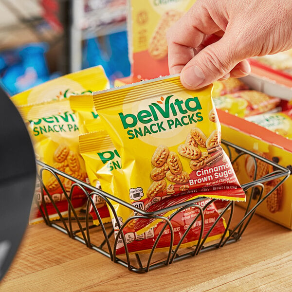 A hand holding a Nabisco belVita Cinnamon Brown Sugar Breakfast Biscuit snack pack.