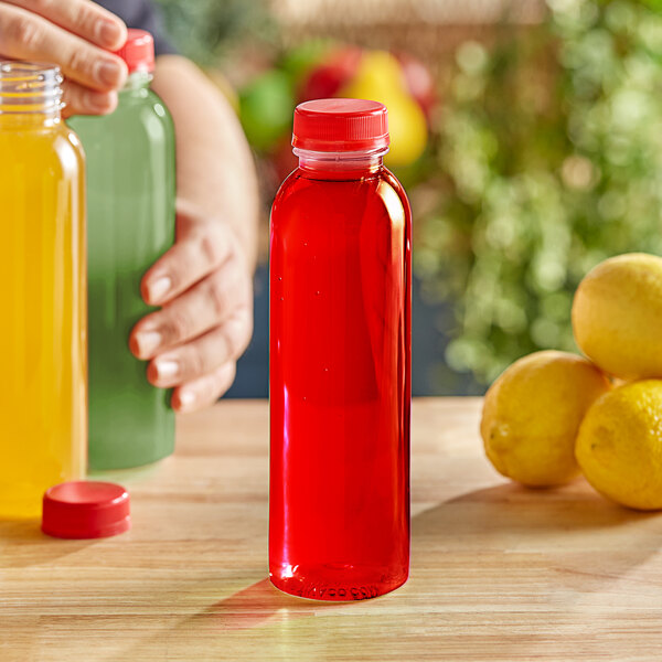 A person holding a 16 oz. round clear PET juice bottle with a red lid.