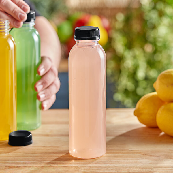 A hand pouring lemon juice into a round clear juice bottle with a black lid.