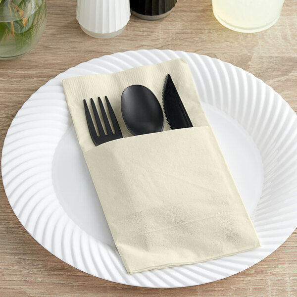 A white square napkin folded around a fork and spoon on a white plate.