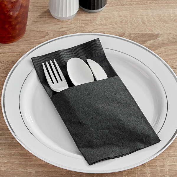 A fork and knife in a black Hoffmaster Quickset dinner napkin on a white plate.