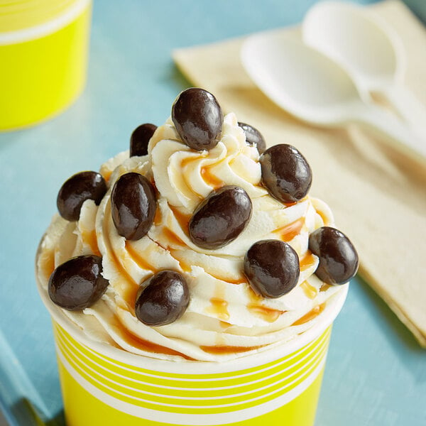 A yellow cup of ice cream with dark chocolate covered peanuts on top.