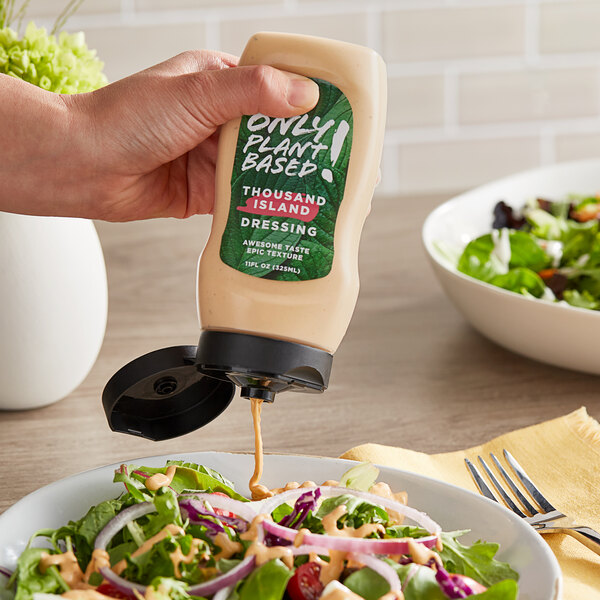 A person pouring Only Plant Based Vegan Thousand Island Dressing onto a salad.