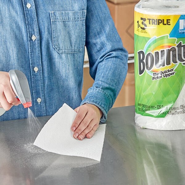 A hand using a spray bottle to clean a counter with a Bounty paper towel.