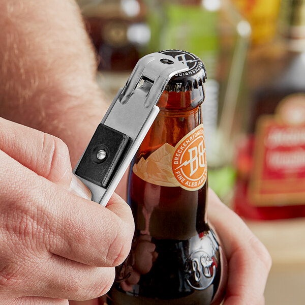 A hand using a Fox Run stainless steel bottle opener to open a bottle of beer.