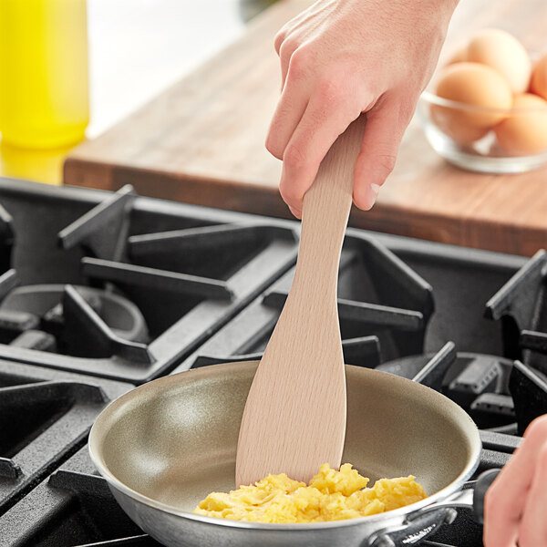 A person using a Fox Run beechwood spatula to cook scrambled eggs in a pan.